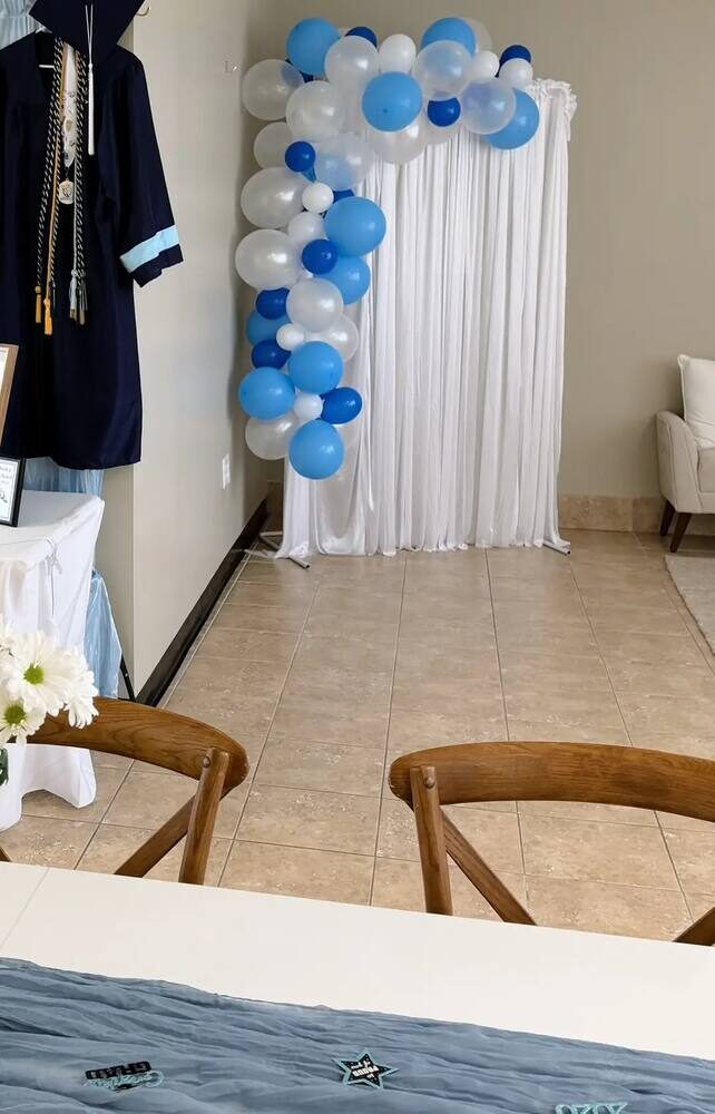 White curtain backdrop with a blue and white balloon garland set up for a graduation party at Simply Social